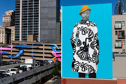 Untitled (Najee S.) — a young woman in a black-and-white patterned coat and mustard hat, painted six stories tall on an electric-blue wall above Sansom Street